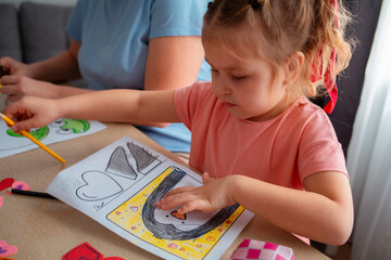 Portrait of little cute girl decorate Valentine's Day cards, sitting at table. Concept of St. Valentine Day and family leisure