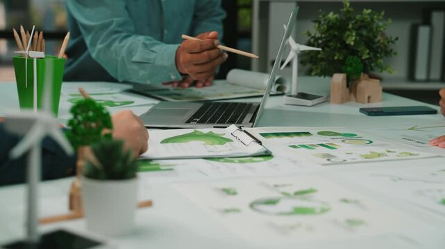 A diverse team in a modern office engaged in discussion, analyzing eco-friendly data and developing sustainable strategies for impactful business growth and environmental care. SACTR - Powered by Adobe