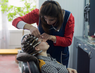 Beautician shapes a young woman’s eyebrows during a salon session. The client wears curlers, preparing for a full beauty transformation in a cozy, professional setting
