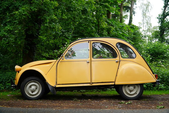 Yellow Citroen 2 CV at the edge of the forest. Mustard yellow vintage object in green nature