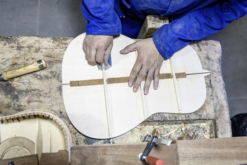 Luthier sanding internal back braces of handmade flamenco guitar in workshop