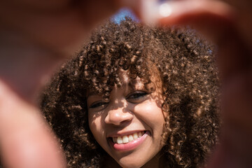 Young woman smiling with curly hair, sunlight filtering through fingers framing her face