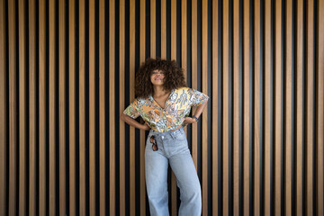 Young stylish woman posing with hands on hips against wooden wall