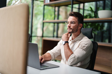Young Caucasian Professional Man In Business Attire Working On Laptop In Contemporary Office Space With Natural Lighting