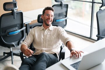Smiling Young Male Professional in Casual Beige Shirt Relaxing in Modern Office Environment