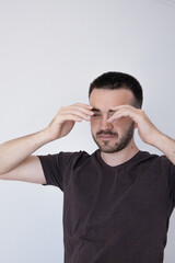 A young man in a casual t-shirt holds his head in both hands with a distressed expression, eyes...