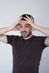 A young man in a casual t-shirt holds his head in both hands with a distressed or surprised...