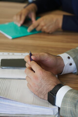 Close up of a businessman’s hands holding a pen over an open notebook during a meeting, ideal for illustrating corporate note-taking, planning and teamwork. Photo
