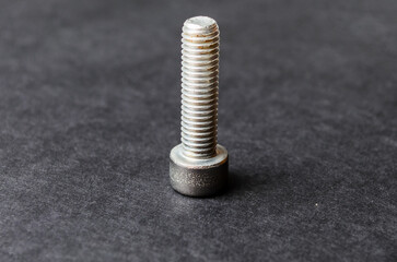 Single old metal bolt standing upright on black background with light