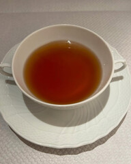 Clear brown soup served in porcelain cup.