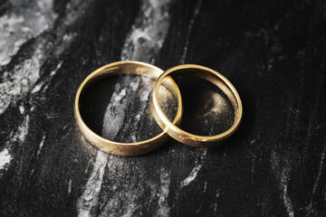 Two gold wedding rings on marble. Symbol of marriage and love. Traditional jewelry closeup. Engagement concept. Classic romantic representation. Shiny yellow gold isolated on black.