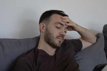 Portrait of a young man in a casual t-shirt sitting on the sofa at home and looking on his phone....
