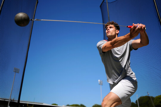 A male athlete focuses on his technique while throwing a hammer at an outdoor training facility under a clear blue sky. Generative AI.