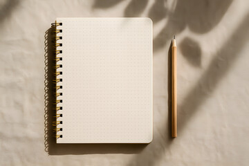 A dotted spiral notebook with a wooden pencil placed on beige fabric, styled with natural shadows and neutral tones..