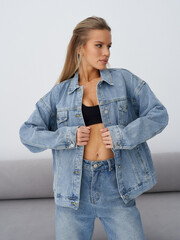 Fashionable individual wearing oversized denim jacket and jeans with a black top, posing...