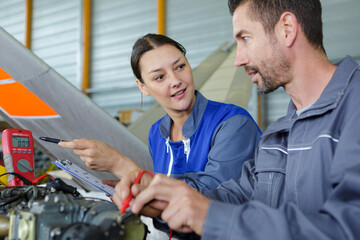 male and female mechanics using multimeter in workshop