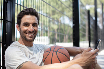 smiling basketball player using mobile phone while taking a break