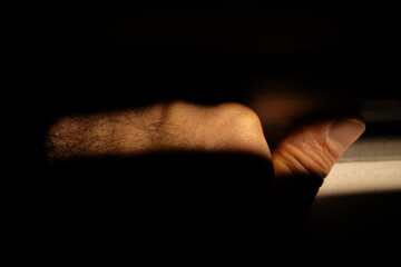 Mão e dedos masculina iluminada pela luz do sol formando um sombra marcante sobre uma mesa de madeira. 