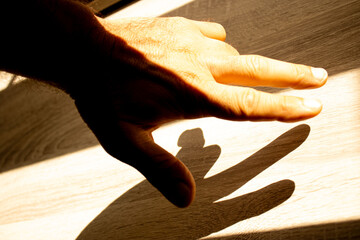 Mão e dedos masculina iluminada pela luz do sol formando um sombra marcante sobre uma mesa de madeira.   © Luiz Leite
