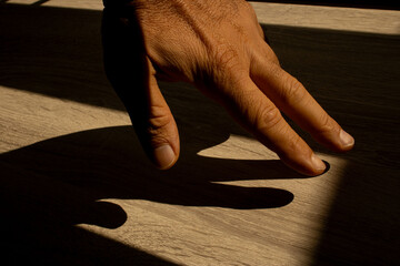 Mão e dedos masculina iluminada pela luz do sol formando um sombra marcante sobre uma mesa de...