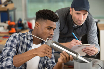 apprentice being advised how to apply caulk