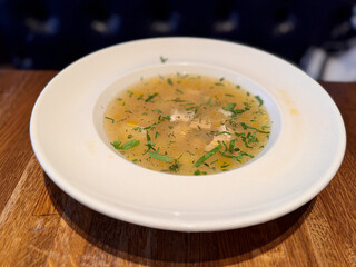 A Truly Delicious Bowl of Soup Elegantly Presented on a Rustic Wooden Table Surface. A warm bowl of savory soup, garnished with herbs, served on a rustic table in a cozy, inviting setting