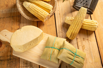 Green corn and pamonha, cobs of green corn, cheese and pamonha and accessories on a rustic wooden...
