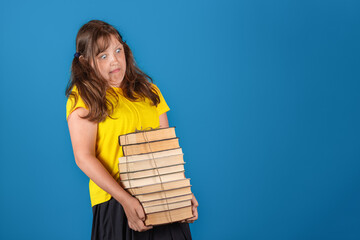 Back to school concept. Young blonde tired teen girl holding huge stack of books against blue background