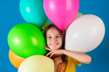 Birthday, party or celebration concept. Cute little european smiling girl makes her way through the balloons on blue background