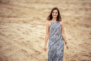 Young beautiful woman walking on sand in desert, looking at camera, smiling