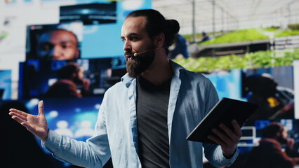 Male cool IT expert hosting a live convention with hands free microphone, engaging an audience from...