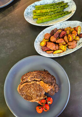 Sirloin steak, fried potatoes and aspargus on plates, top view