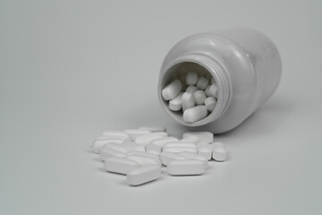 White pills tablets spilled from a bottle on a light grey background 