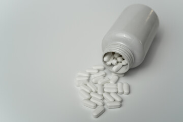 White pills tablets spilled from a bottle on a light grey background 