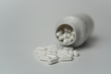 White pills tablets spilled from a bottle on a light grey background 