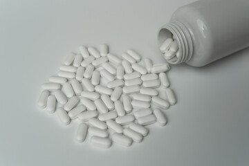 White pills tablets spilled from a bottle on a light grey background 