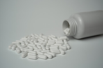 White pills tablets spilled from a bottle on a light grey background 