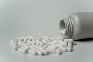 White pills tablets spilled from a bottle on a light grey background 