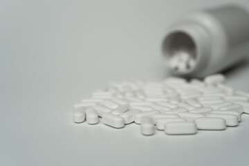 White pills tablets spilled from a bottle on a light grey background 