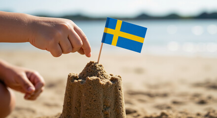 Child hand placing Swedish flag on sandcastle at the beach. Summer vacation fun, childhood play and patriotism concept. Building sand castle on beach in Sweden. National day in Sweden. 6 June.