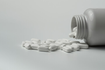 White pills tablets spilled from a bottle on a light grey background 