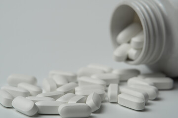 White pills tablets spilled from a bottle on a light grey background 