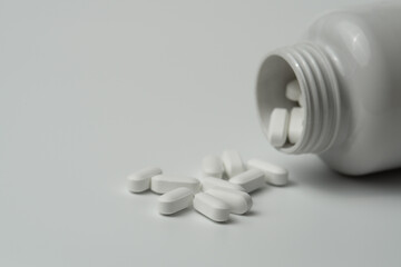 White pills tablets spilled from a bottle on a light grey background 