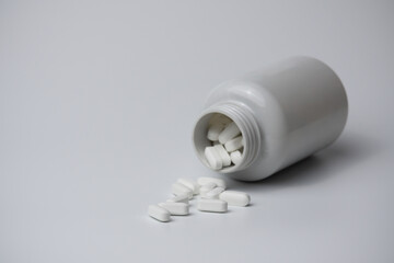 White pills tablets spilled from a bottle on a light grey background 