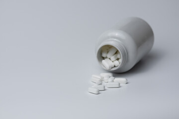White pills tablets spilled from a bottle on a light grey background 