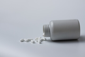 White pills tablets spilled from a bottle on a light grey background 