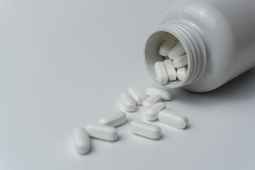 White pills tablets spilled from a bottle on a light grey background 