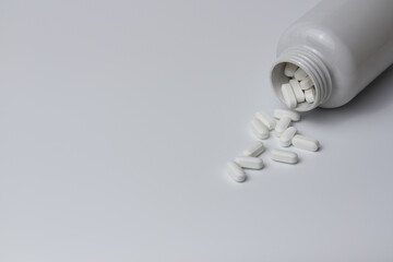White pills tablets spilled from a bottle on a light grey background 