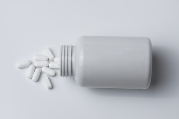 White pills spilled from a bottle on a light grey background top view