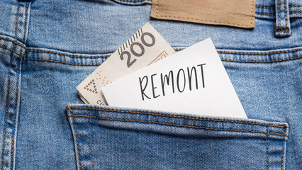 White card with a handwritten inscription "Remont", put into the pocket of blue pants jeasnow, next to Polish banknotes PLN (selective focus), translation: Renovation